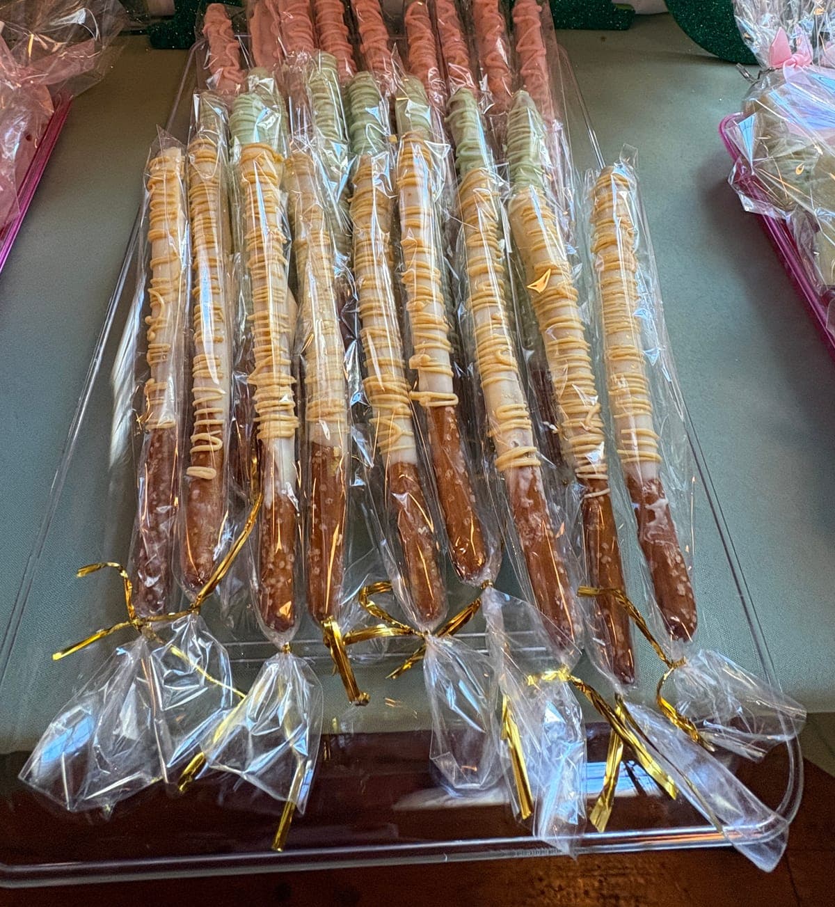 Tray of chocolate-covered pretzel rods with drizzle in three colors, each wrapped and tied with a gold twist