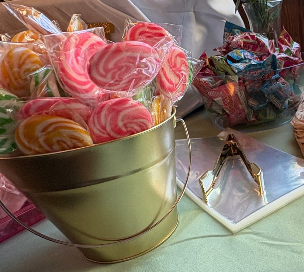 Gold pail filled with pink, orange and green swirl lollipops on a candy buffet
